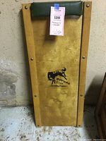 Full view of wooden mechanic creeper with attached tag showing lot number and partial description, creamer has padded headrest and visible wear marks.