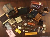 Full lot of miscellaneous men's accessories including knives, cufflinks, tie clips, carved wood figurine, leather goods, advertising items, and collectibles shown on wooden table