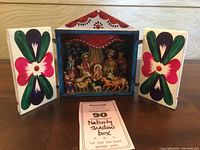 Closed shadow box showing outward-facing doors painted with large colorful flower designs and a red peaked roof with decorative pattern and chip on peak.