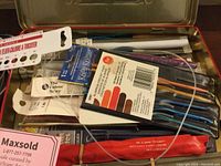 Top view of knitting needles and needle kits with original packaging inside a metal tin box.