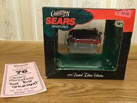 Photo of original green and red cardboard box with clear window showing the Sears mini tool box ornament inside. Shows price stickers $2.99 and $4.99 on box corners.