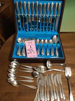 Overview of open wooden case showing interior flatware and additional pieces on table