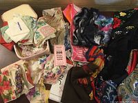 Photo showing assortment of scarves, wraps, and vintage handkerchiefs spread out on table.