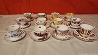 Photo showing all twelve assorted porcelain teacups with matching saucers arranged in rows against an orange background.