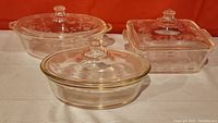 Three clear Pyrex glass covered casserole dishes shown with decorative floral etched lids - one large square and two round dishes