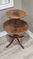 Full view of antique two-tier side table showing pie crust scalloped edges on the tabletop surfaces and wooden pedestal base with four legs.