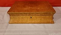 Closed antique wooden jewelry box showing the top decorated lid and front side with keyhole but no key
