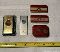Top view of two vintage gold-tone cigar cutters and three small vintage tins of Full Tone Victrola needles arranged near a measuring tape for size reference