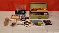 Fishing tackle lot laid out with box, lines, flies, lures and packaged hooks.