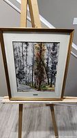 Full view of framed painting on easel showing fall tree and wooded pathway.