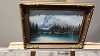 Framed landscape pastel painting showing mountains, trees, and lake with an ornate frame.