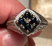 Close-up view of the ring face showing four blue sapphire stones set in a square cluster with ornate silver design on the band sides.