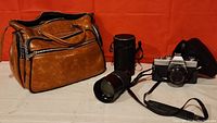 Full view showing brown camera bag, 200mm zoom lens with attached strap, lens case, and Minolta SRT200 camera body.