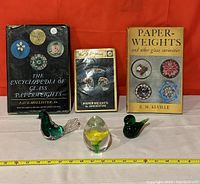 Glass paperweights and three books displayed side by side on a surface with measuring tape showing scale.