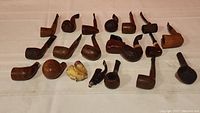Overview of lying down smoking pipes showing various shapes, sizes, and finishes laid on white fabric background.