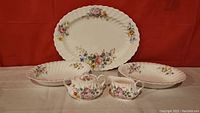 Full view of the set showing large oval platter, two oval serving dishes, covered sugar bowl, and creamer with floral pattern.