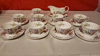 Full set of 8 tea cups and 8 saucers arranged with sauce boat visible in background, showing overall lot contents and condition
