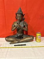 Front view of seated Buddha statue with detached flute and scale reference