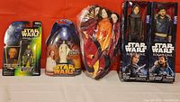 Four Star Wars action figures in original packaging and three porcelain dolls wrapped in plastic on an orange/red background.