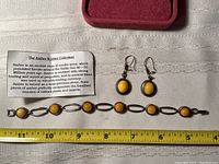 Photo showing the earrings and bracelet laid out on fabric next to a measuring tape and a description card about amber.