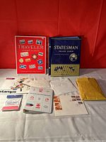 Wide shot displaying two stamp albums (Traveler and Statesman Deluxe) and multiple envelopes and stamp packets laid out on a table.