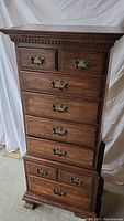 Full view of the tall wood lingerie chest showing 7 drawers with brass handles, crown molding at the top and bracket feet