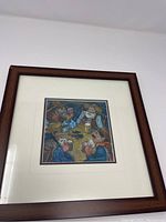 Framed art card depicting cowboys playing cards around a table with drinks, in earthy tones.