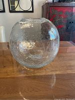 Side view of the crackle glass globe on a wooden table showing its round shape and crackled texture.