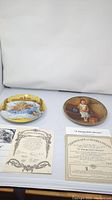 Two collectible decorative plates and their certificates of authenticity displayed side by side on a plain white surface.