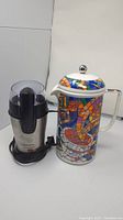 Photo showing the Second Cup French press with colorful mosaic coffee cup pattern beside the Black & Decker Smart Grind coffee grinder with visible power cord.