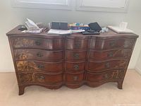 Front view of mid century wooden dresser with curved drawers and decorative floral inlay.