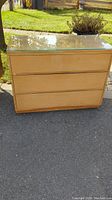 Front view of wooden Mid-Century Modern dresser with glass top showing three drawers.