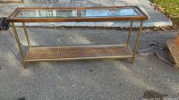 Full view of rectangular mid-century modern console table with glass top on paved surface outdoors.