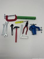 Full view of all miniature tools displayed on white surface including wrenches, hammer, pliers, level, vise, C-clamp, and corner ruler with a Sharpie pen for scale comparison.