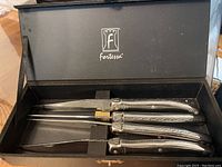 Four Fortessa serrated steak knives with decorative handles arranged in original black Fortessa box.