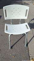 Front view of the lightweight ergonomic shower chair showing white textured plastic seat and backrest with drainage holes and aluminum legs.
