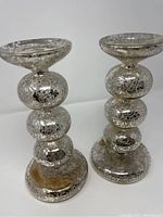 Pair of tall glass candleholders with metal accents, showing front and side views with visible wax residue and some discoloration.