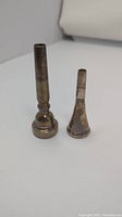 Two brass instrument mouthpieces side by side showing relative size and patina wear