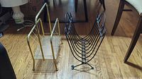 Photo showing both brass and black metal magazine stands on a wooden floor.