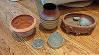 Photo of all items on wood floor: three plant pots (two terra-cotta, one ceramic) and two small clear glass flower holder inserts