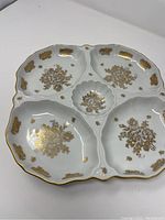 Top view of white porcelain serving tray with five divided sections decorated with golden floral patterns and scalloped edges.