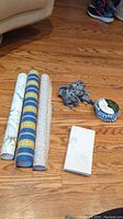 Three rolls of wallpaper, two fabric trims, and a stack of handmade envelopes on a wooden floor
