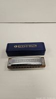 Blues Harp MS harmonica placed on white surface beside its blue plastic case with gold logo.