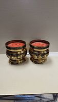 Pair of brass electric incense burners showing front and side views with red perforated tops and gold decorative designs