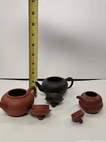 Three small ceramic teapots shown together with lid and handle details. Black one has a chip on lid, tiny one has broken handle, reddish-brown one appears intact.