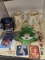 Overview of assorted Christmas-themed items including pitcher jars, porcelain figurines, dish, gift card holders, and a book.