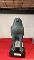 Front view of the dark Horus falcon statue on a rectangular base with visible glued crack on the beak.
