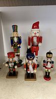 Set of 5 nutcracker figurines displayed on a surface, varies in color and size, includes four wooden and one resin nutcracker.