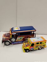 Front and side view of two colorful vintage Philippine jeepney toy models, one large and one small, showcasing detailed paint and chrome features.