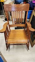 Front view of a wooden rocking chair with a slatted backrest and curved armrests showing the overall shape and condition.